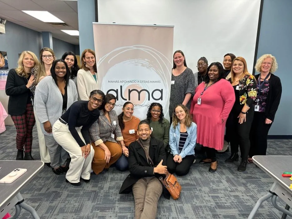 Large group of people posing in front of Alma banner and smiling.