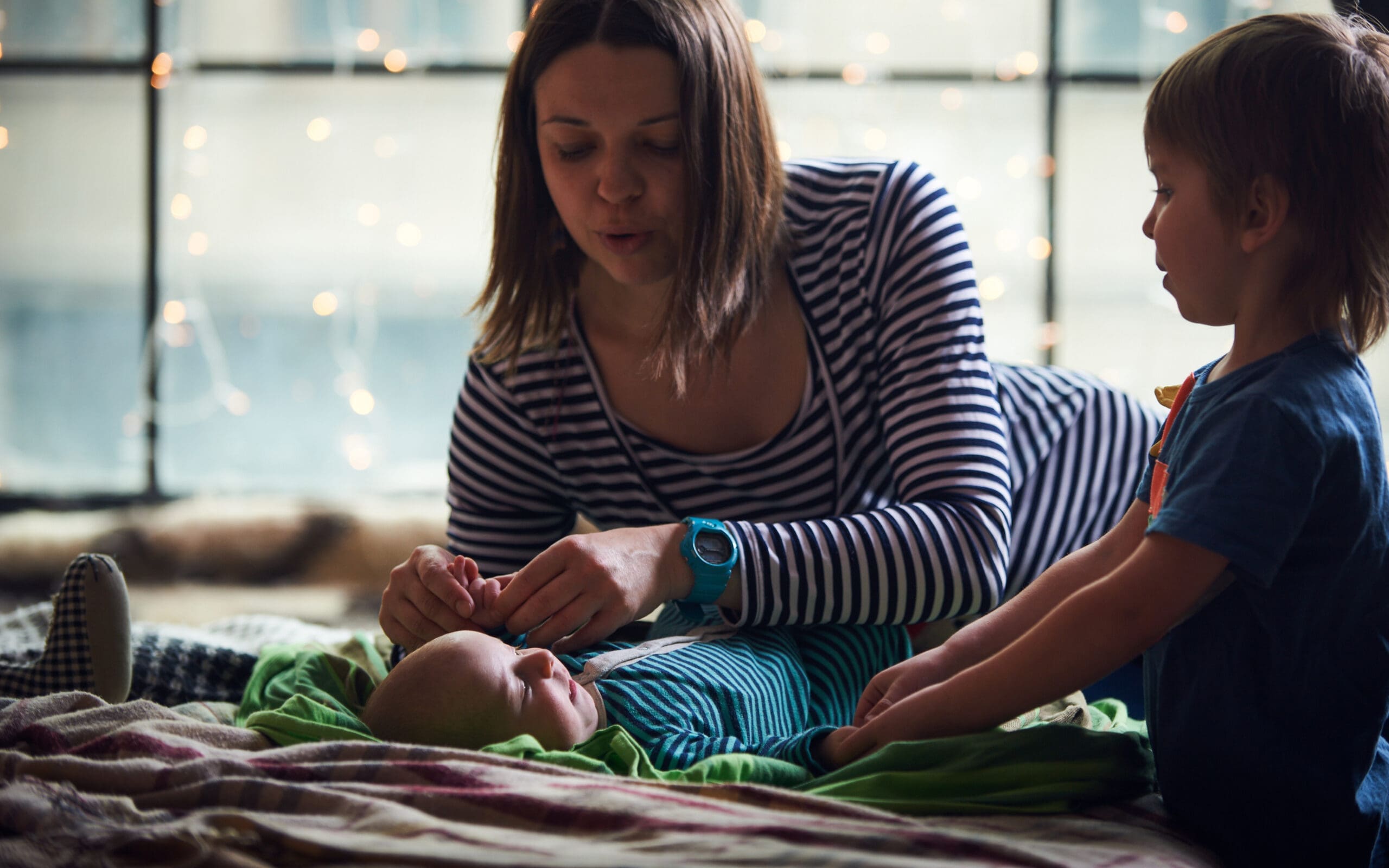 Mother and young child caring for infant on a bed.