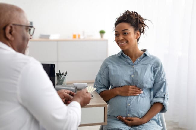 Smiling pregnant person with hands on belly listening to doctor giving instructions.